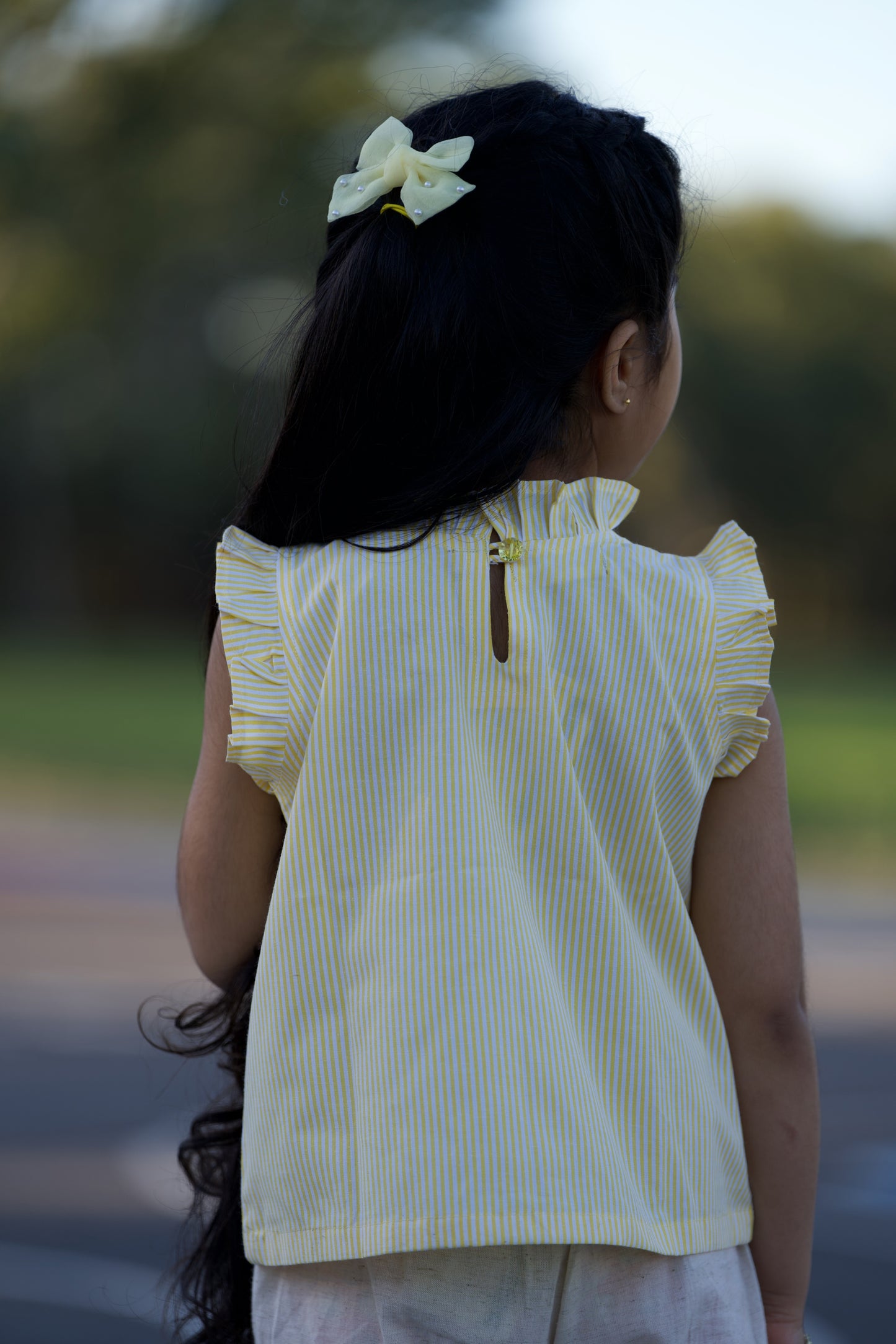 Young girl wearing a yellow striped shirt with a blurred outdoor background