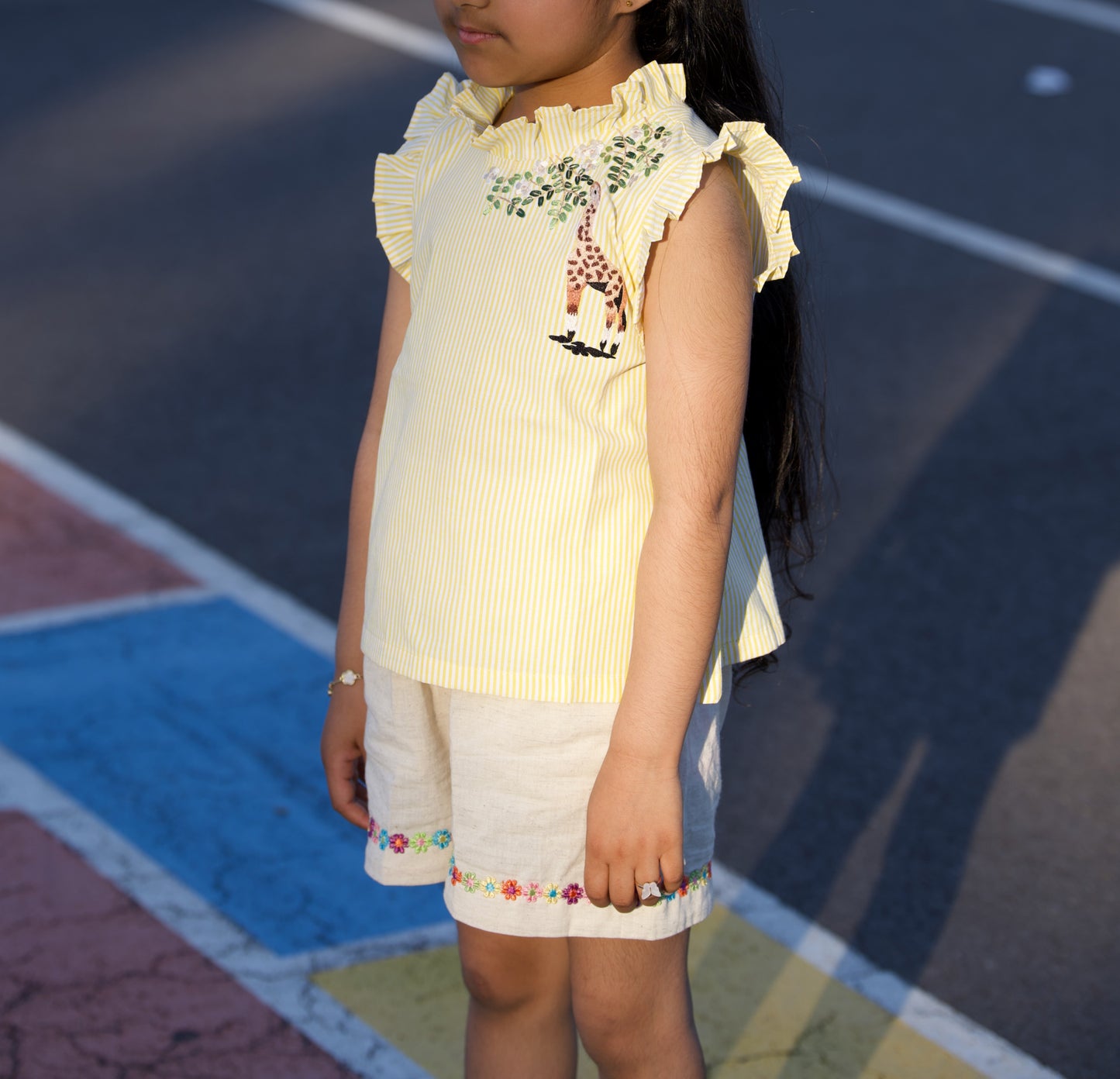Young girl wearing a yellow top and white skirt with embroidery, standing on a colorful pavement.